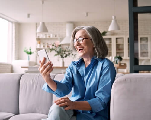 A woman smiling while she browses the web on her phone.